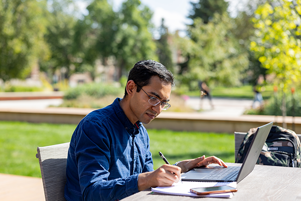 Man researching on his computer at an outdoor table on campus